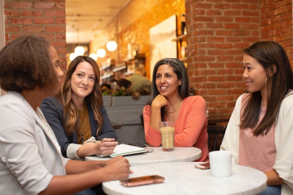 Four women converse while sitting around a table.